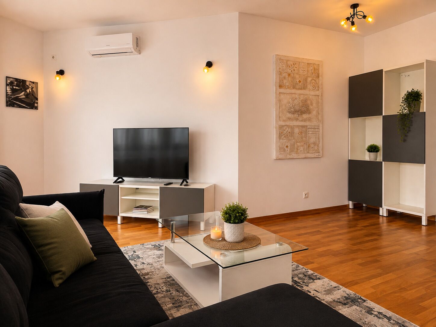 Una sala de estar moderna con un televisor de pantalla plana, una mesa de centro de vidrio, un sofá negro y un estante minimalista.