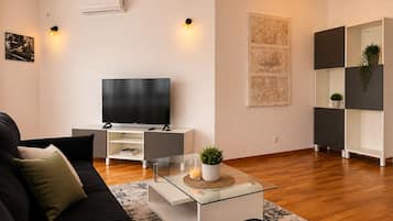 Una sala de estar moderna con un televisor de pantalla plana, una mesa de centro de vidrio, un sofá negro y un estante minimalista.