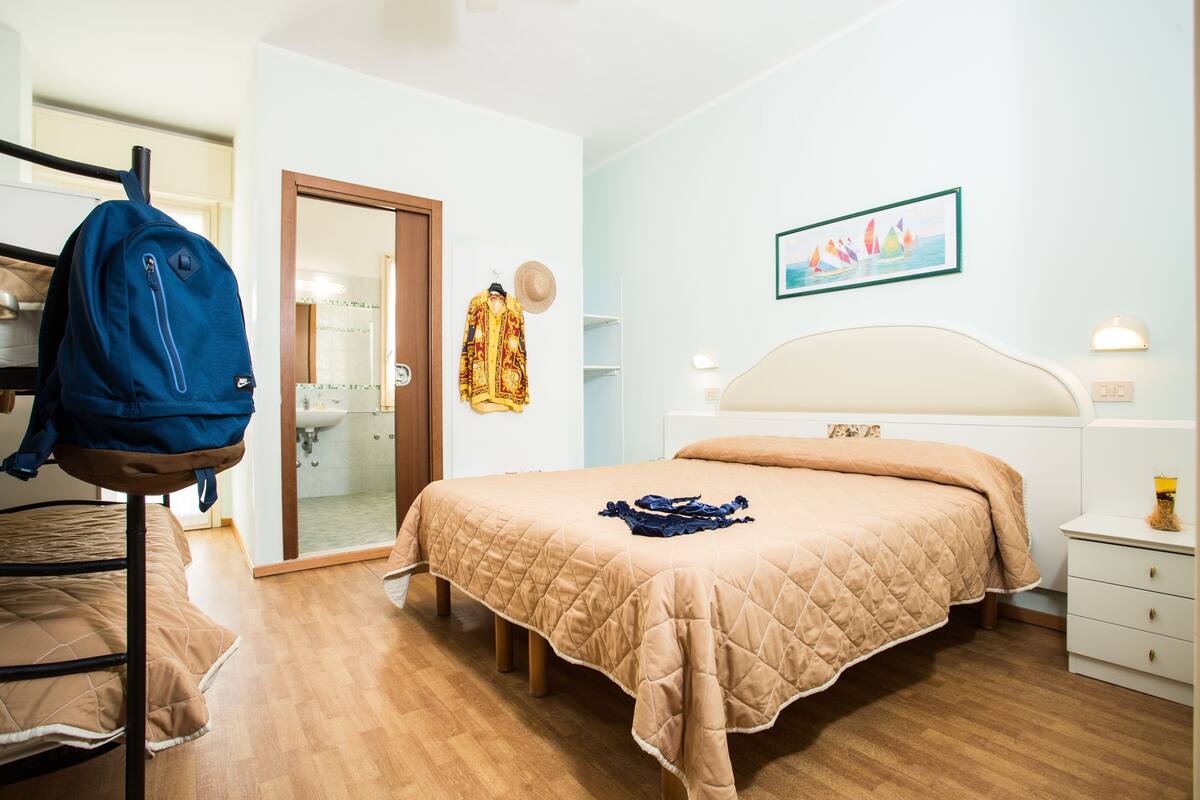 A bedroom with a bed, a wardrobe, a mirror, and a bathroom visible through an open door.