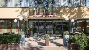 A hotel entrance with a balcony, potted plants, and a sign reading "SALUTE OSPITE GRADITO". - Hotel Club Misano (Misano Adriatico)