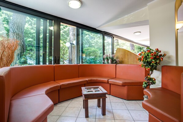 Un salon moderne avec un canapé orange aux lignes courbes, une petite table basse en bois et une grande fenêtre donnant sur des arbres et de la verdure.