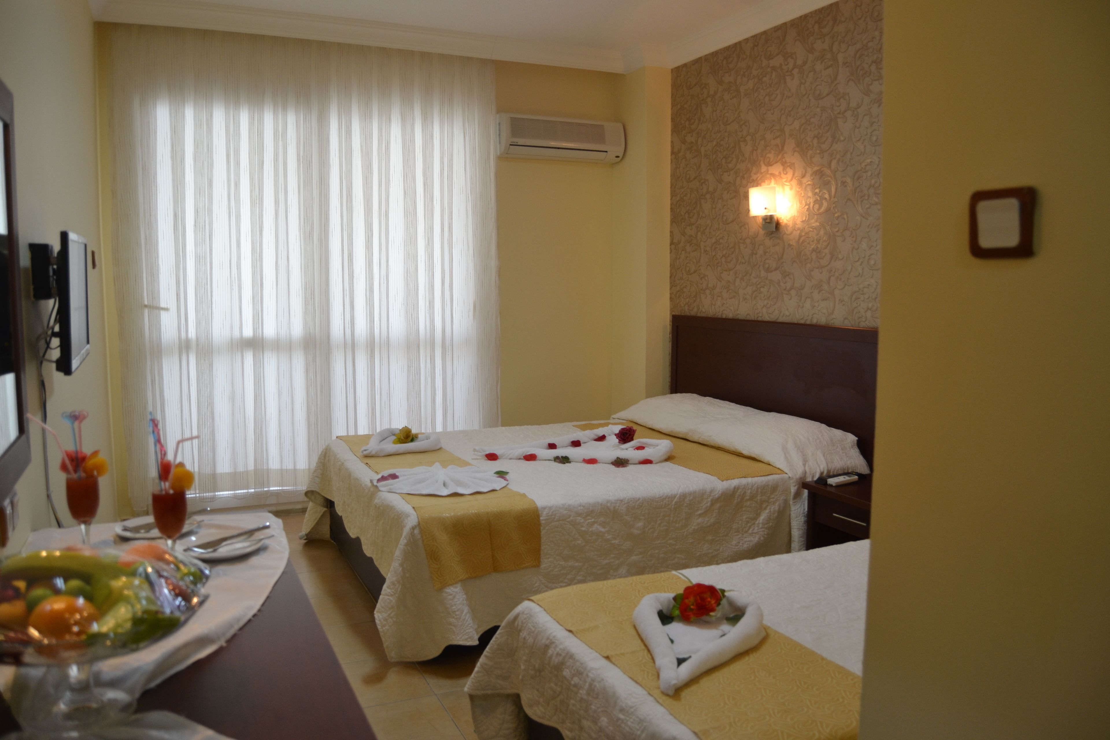 A hotel room with two beds, a dining area with a fruit bowl, and a wall-mounted air conditioner.