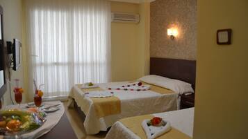 A hotel room with two beds, a dining area with a fruit bowl, and a wall-mounted air conditioner.