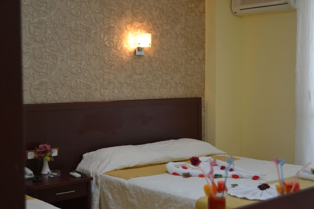 Une chambre d’hôtel comprenant un lit, une table de chevet, une lampe fixée au mur et un panneau décoratif mural.