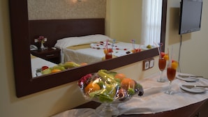 Habitación de hotel con cama, un espejo grande, un frutero y una mesa con vaso de jugo y vaso de agua.