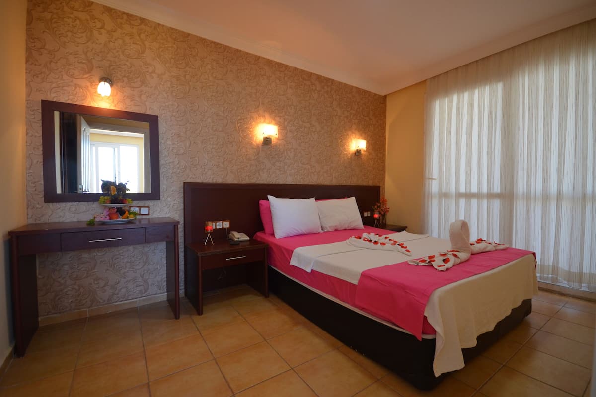 Une chambre d’hôtel avec un grand lit, un bureau, un miroir et deux lampes fixées au mur.