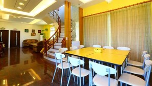 Un comedor con una mesa amarilla y sillas blancas, una escalera y una barandilla.