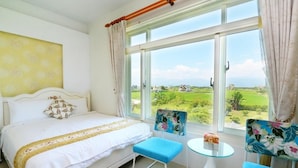 Un dormitorio con una cama, una mesita pequeña, dos sillas y un ventanal con vistas a un paisaje verde.