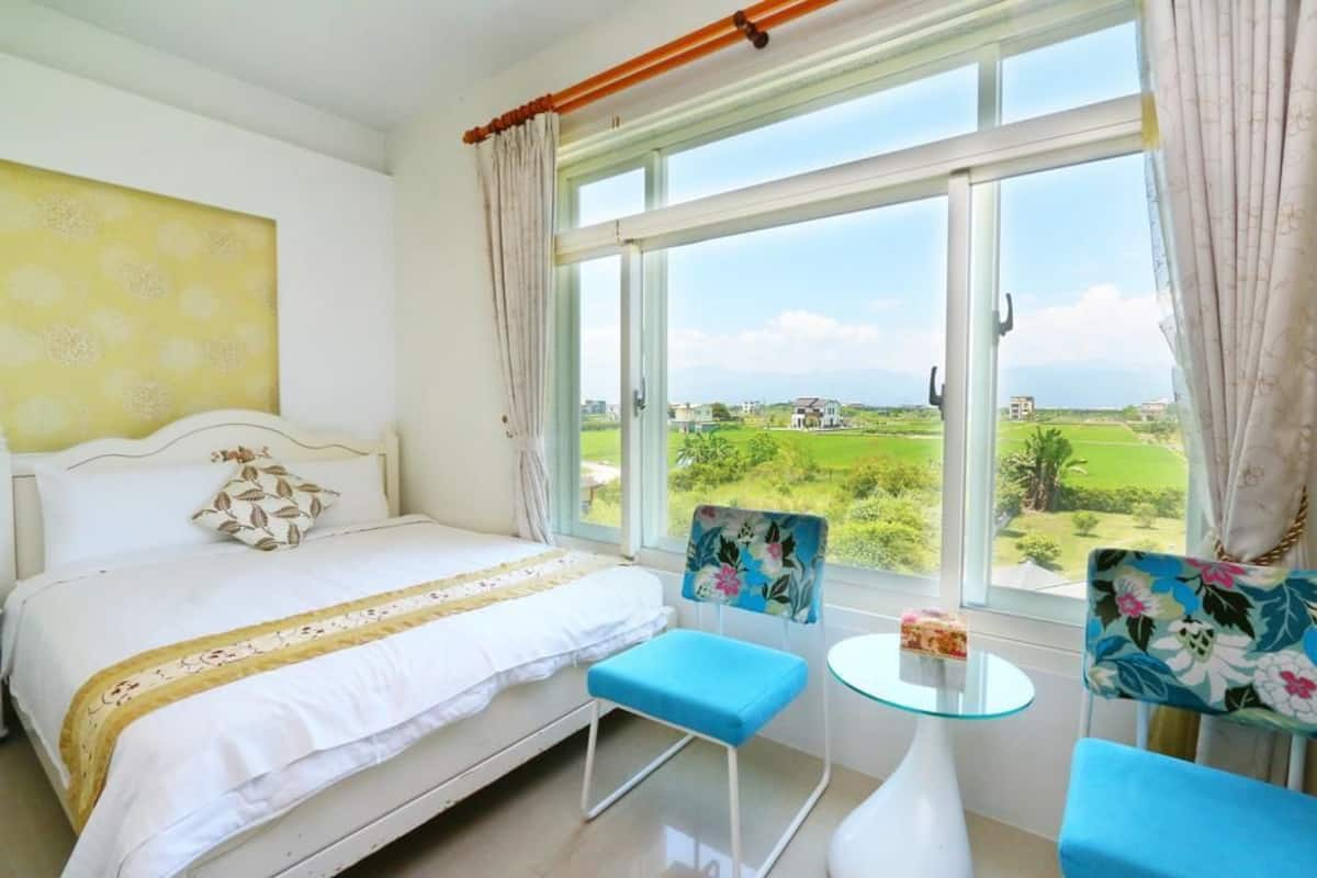 Un dormitorio con una cama, una mesita pequeña, dos sillas y un ventanal con vistas a un paisaje verde.