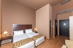 Ett hotellrum med två sängar, ett nattduksbord med en lampa, ett skrivbord och en dörr.