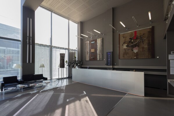 A modern reception area with a glass partition, a reception desk, and a large window offering a view of the cityscape. - Art Hotel Olympic (Turin)