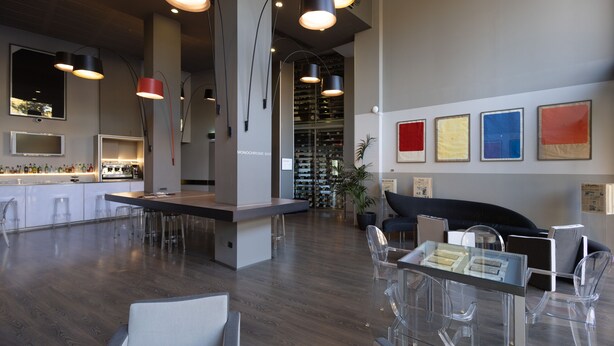 A modern kitchen with bar stools, a dining area with clear chairs, and a wine rack in the background. - Art Hotel Olympic (Turin)