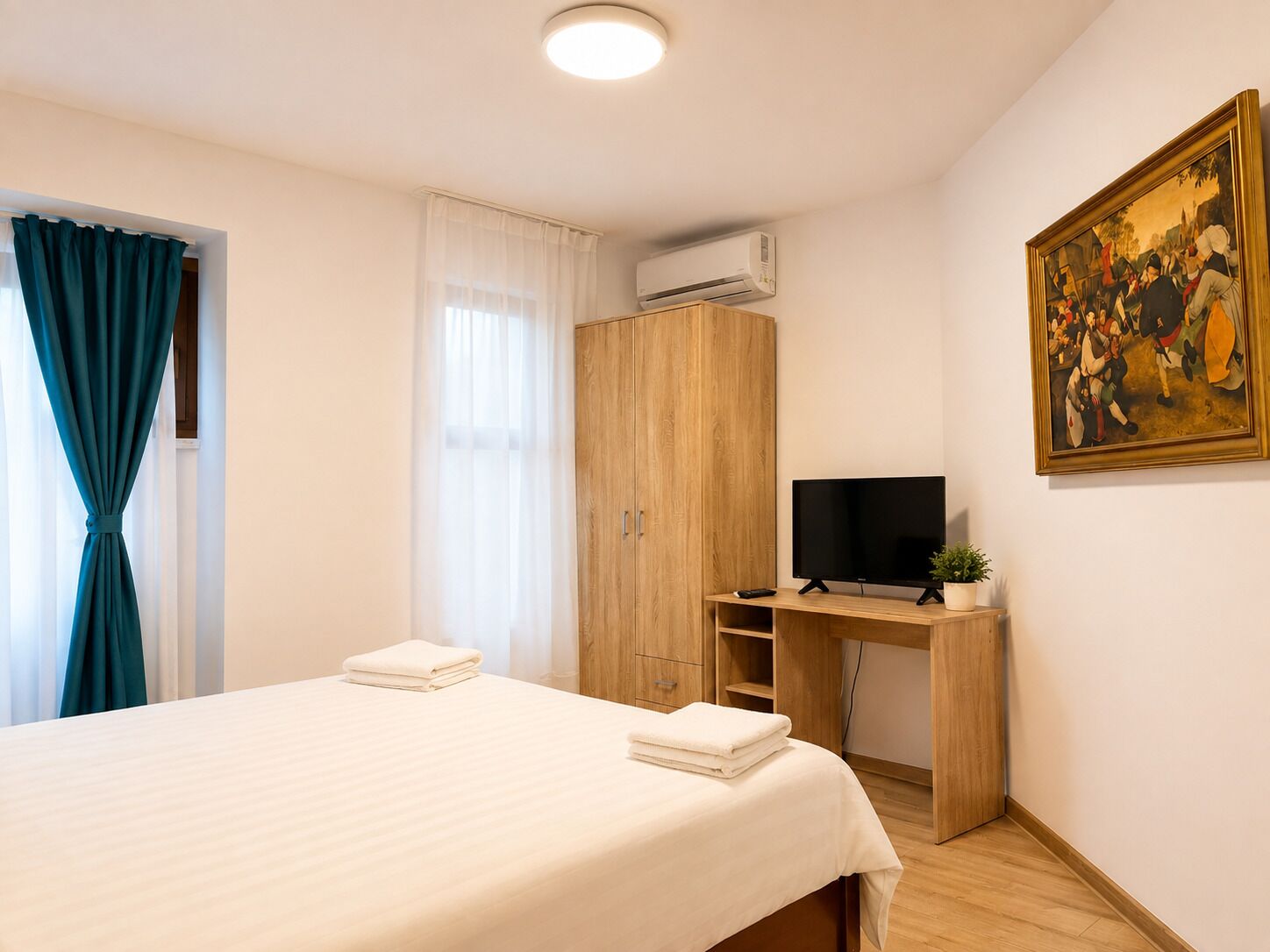 Habitación de hotel con cama, escritorio con televisor, armario y un cuadro en la pared.