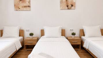 Ein Hotelzimmer mit drei Betten, jeweils mit weißer Bettwäsche und Holz Kopfteilen. Über den Betten hängen zwei an der Wand befestigte Kunstwerke.