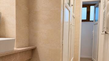 A bathroom with a sink, a shower, and a door leading to another room.