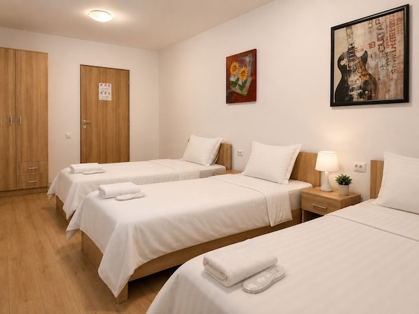 Habitación de hotel con tres camas individuales, un armario de madera, una puerta con un letrero y un cuadro en la pared.