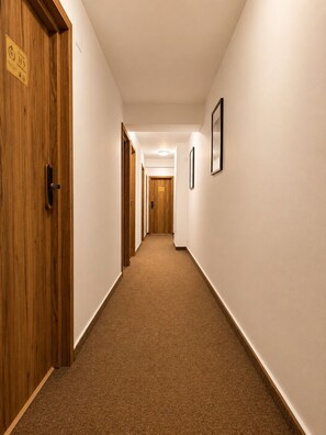 A hallway with wooden doors, a carpeted floor, and framed pictures on the walls. - Monte Carlo Palace Rooms  (Bucharest)