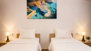 A hotel room with two beds, a painting of a coastal landscape, and bedside lamps.