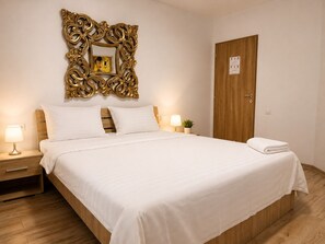 Habitación de hotel con una cama grande, cabecera de madera, dos mesitas de noche con lámparas, una puerta de madera y un espejo decorativo con marco dorado en la pared.