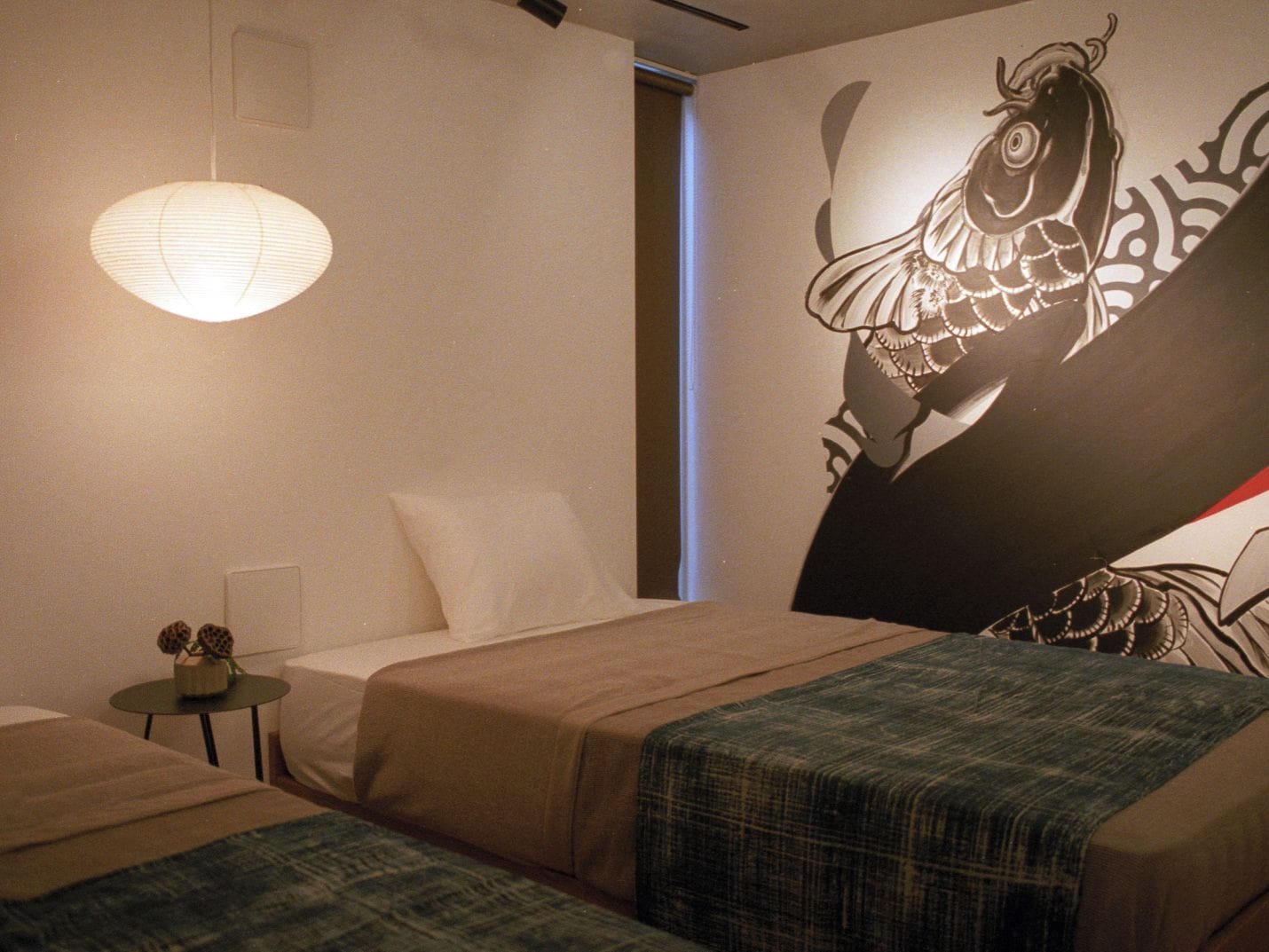 A hotel room with a bed, a small table with a lamp, and a wall with a large bird mural.