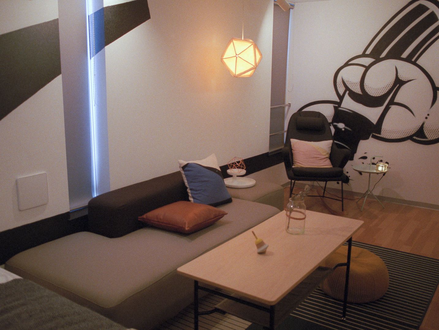 A modern living room with a sofa, a coffee table, and a chair. There is a wall art piece and a hanging light fixture.
