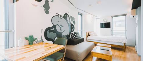 A modern bedroom with a bed, a desk, and a chair. There is a wall mural with a cartoon character.