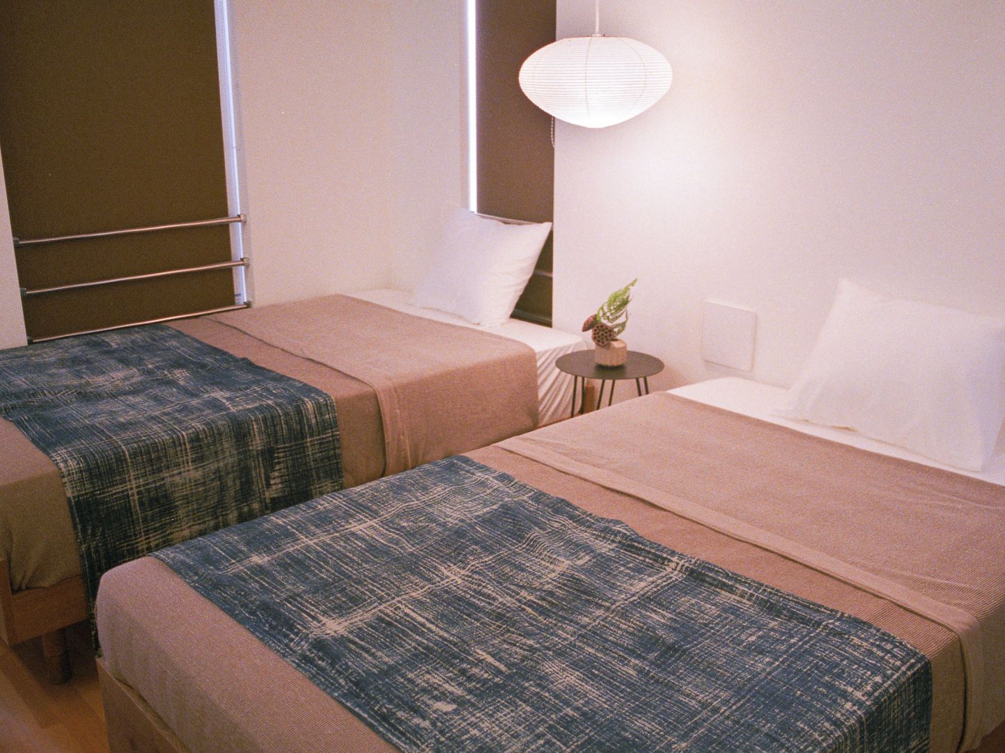 A hotel room with two beds, a small table with a plant, and a wall-mounted lamp.