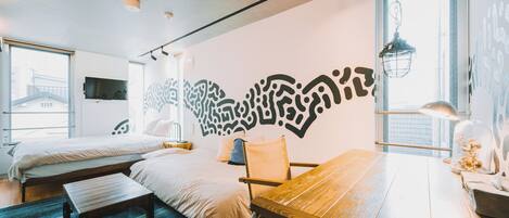 A modern hotel room with two beds, a dining table, a large window, and a decorative wall mural.