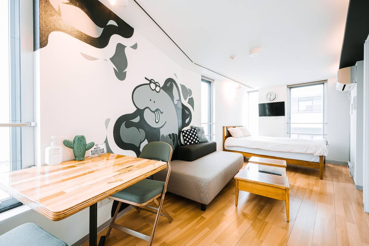 Une chambre moderne avec une table à manger en bois, un canapé gris, un lit et une fresque murale.