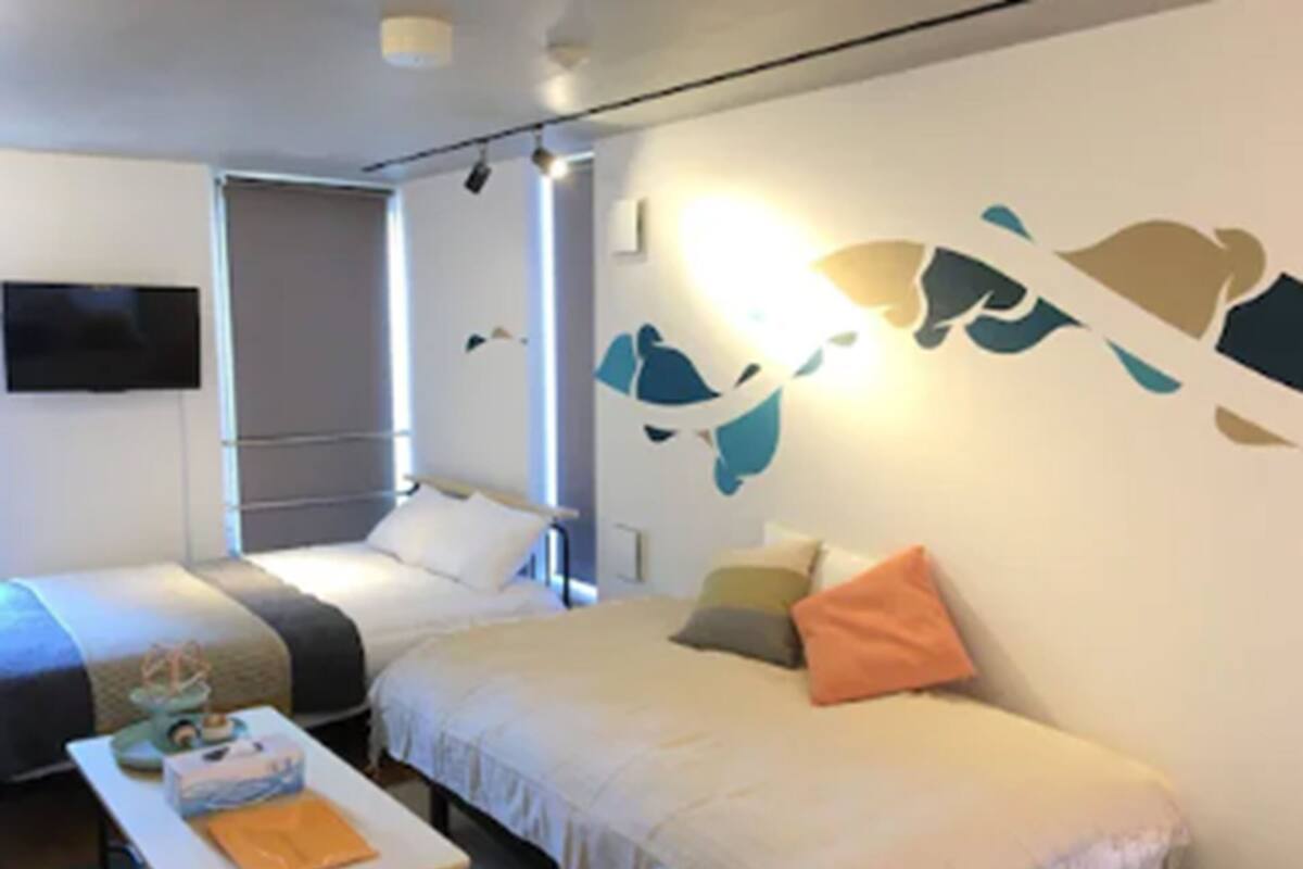 Une chambre d’hôtel avec deux lits simples, une petite table avec une lampe et un téléviseur fixé au mur.