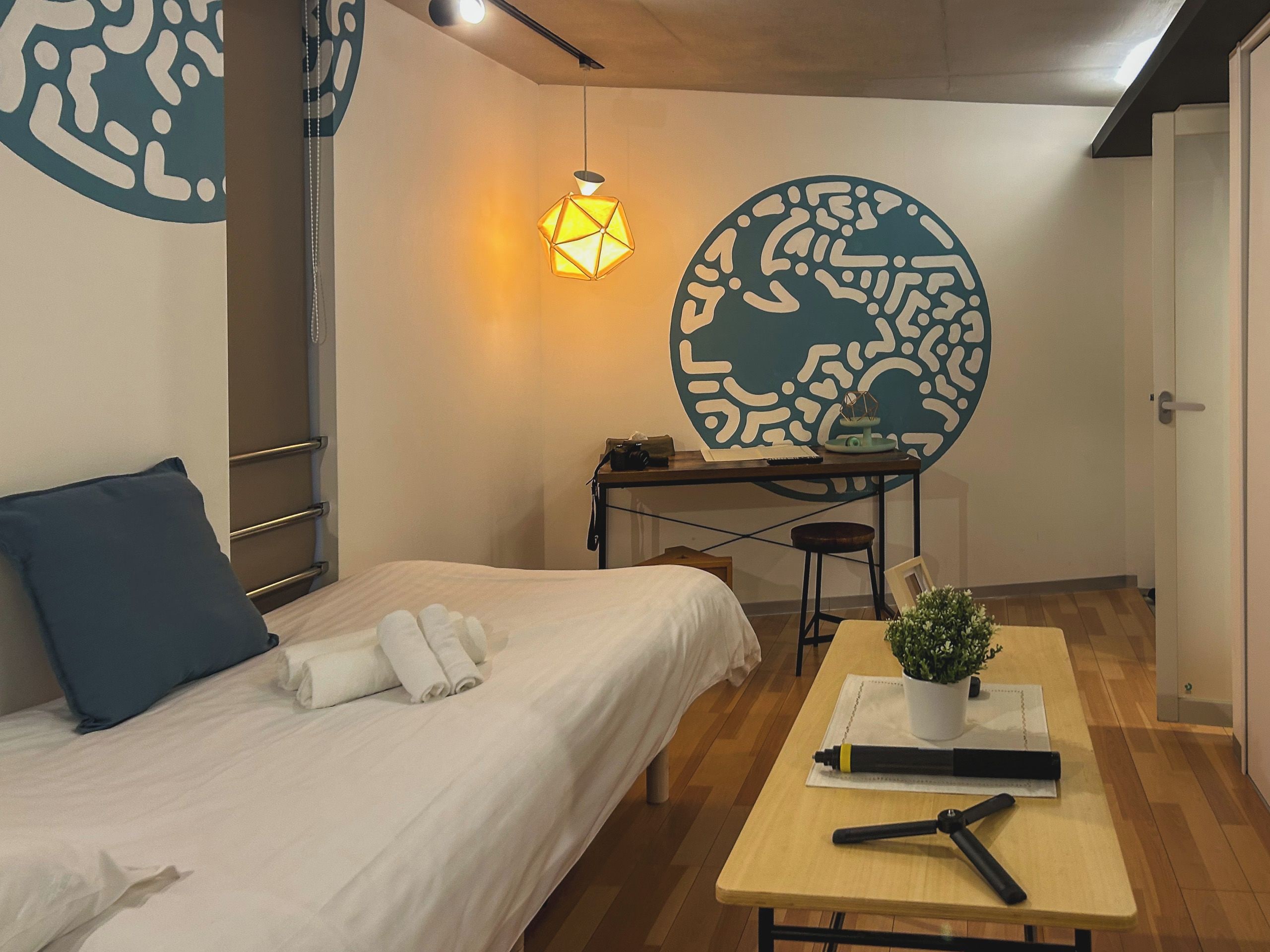 A modern hotel room with a bed, a desk, a lamp, and a wall art piece.