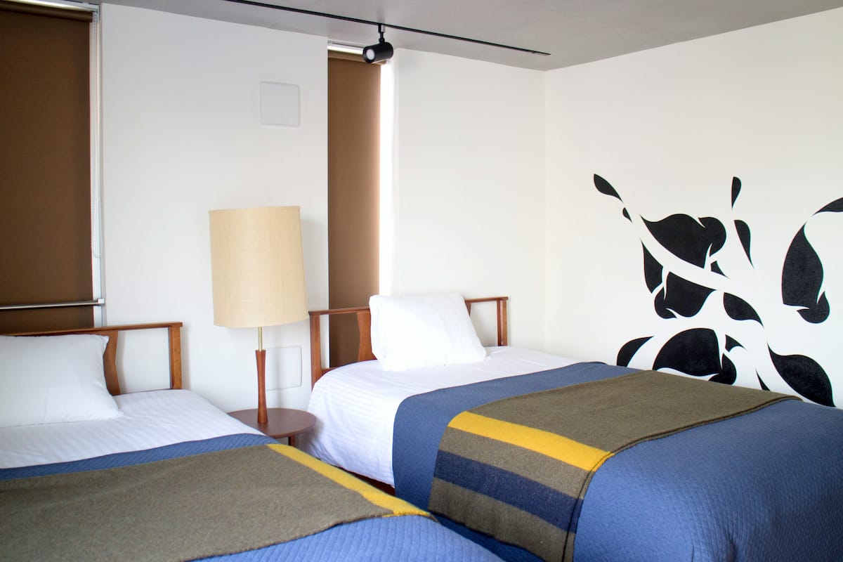 Une chambre d’hôtel avec deux lits, une lampe et un mur orné d’un motif abstrait en noir et blanc.
