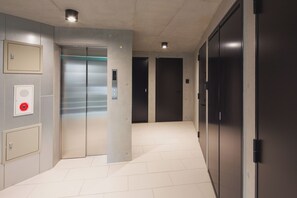 A corridor with two elevators, a fire alarm, and a door with a red emergency button. - THE AOCA TOKYO SANNO (Tokyo)