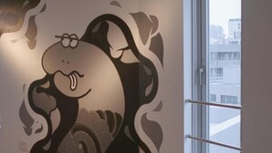 Un mur orné d’un motif animal stylisé, une fenêtre dotée d’une poignée en métal et une vue sur les bâtiments à l’extérieur.