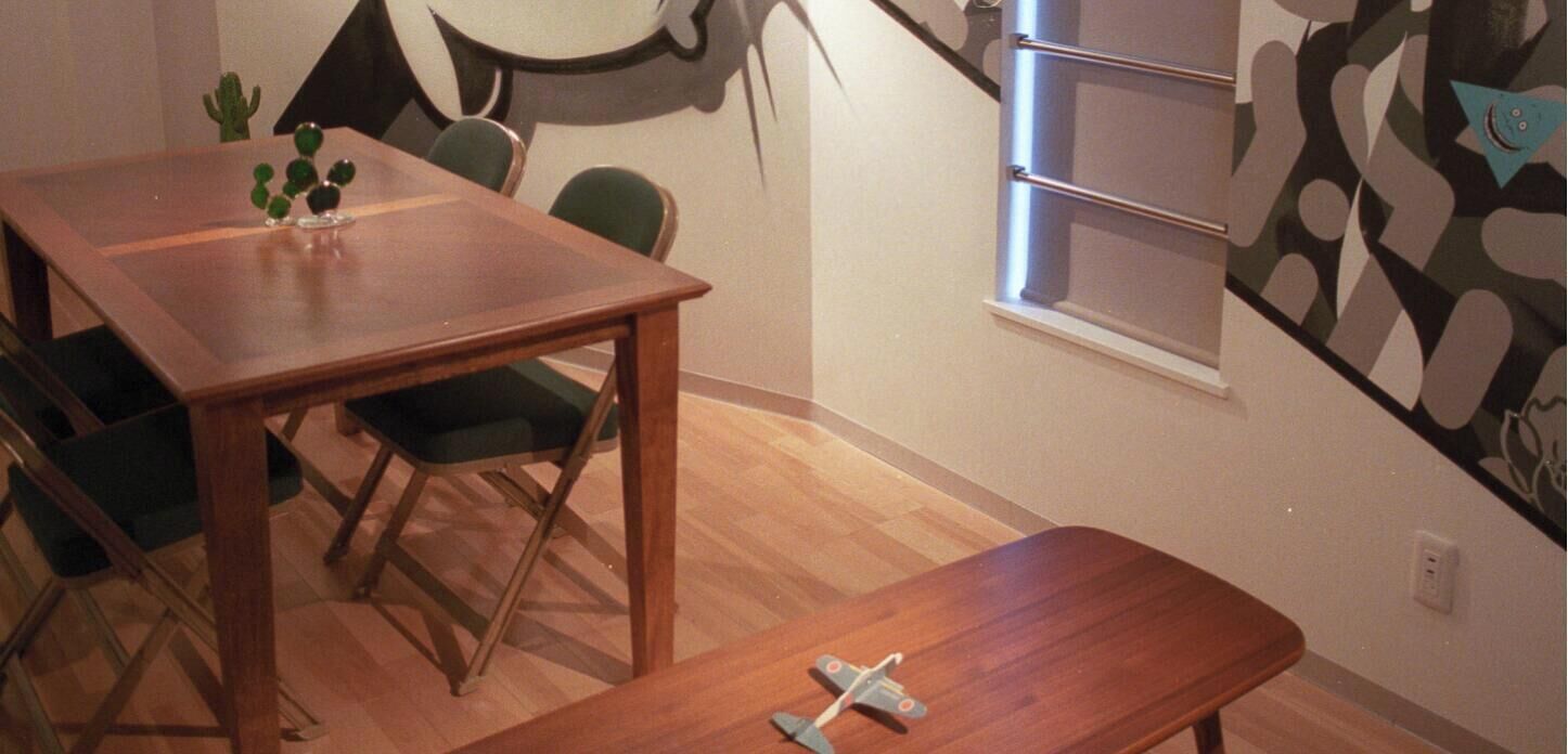 A room with a wooden dining table, two chairs, a small cactus plant, and a toy airplane on the floor.