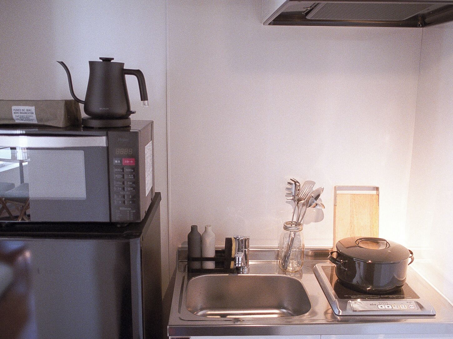 Una cucina con microonde, bollitore, lavello e una pentola su un piano cottura a induzione.
