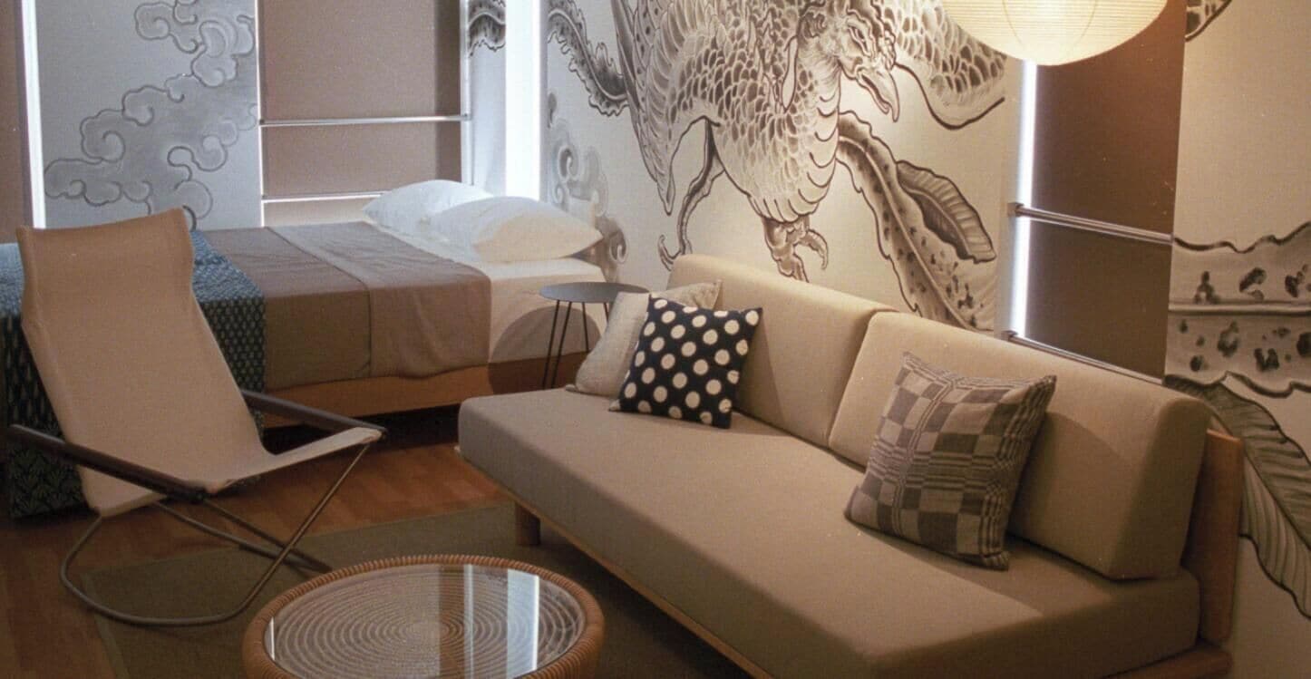 A modern hotel room with a bed, a sofa, a chair, and a round table.