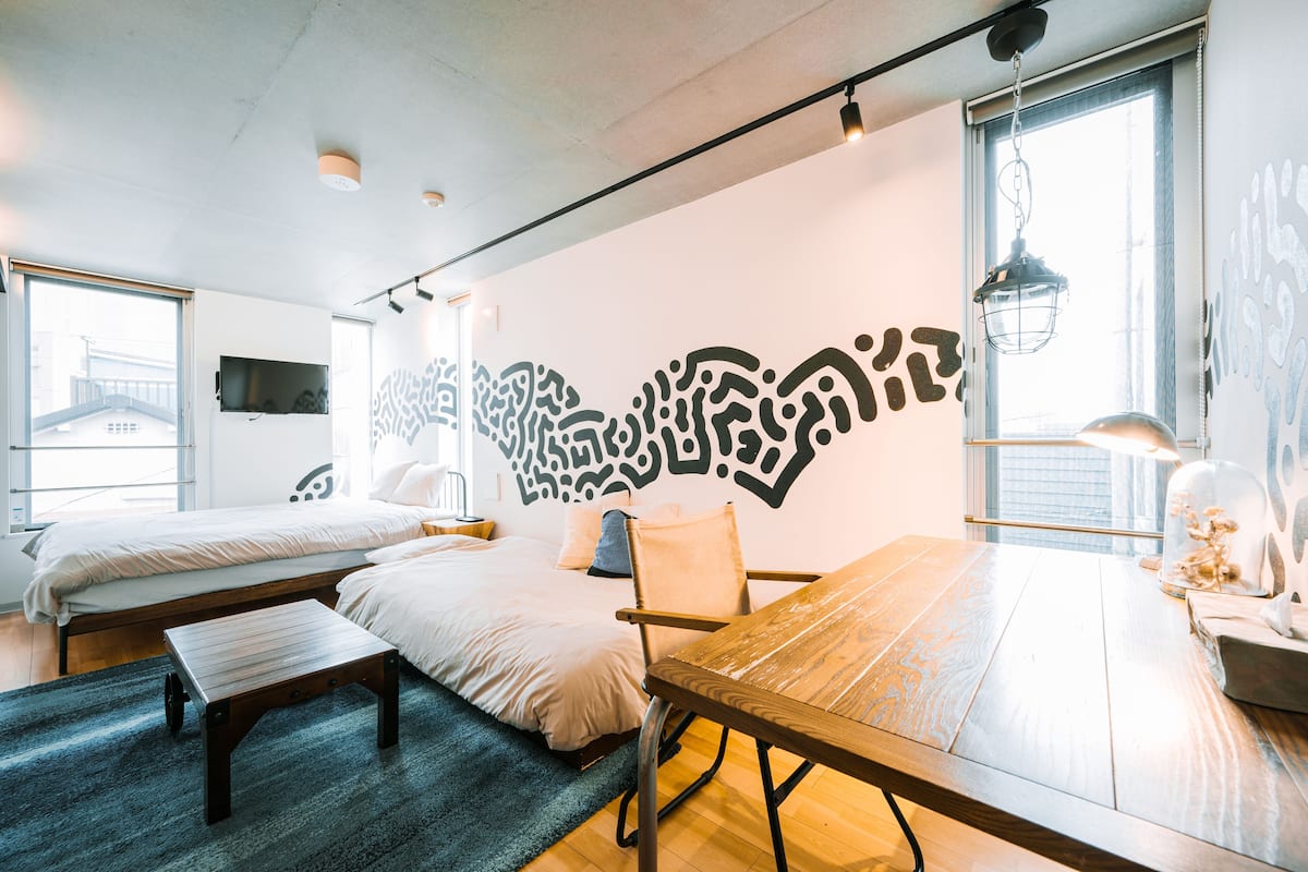 Une chambre moderne avec une grande table en bois, deux lits et un décor mural original.