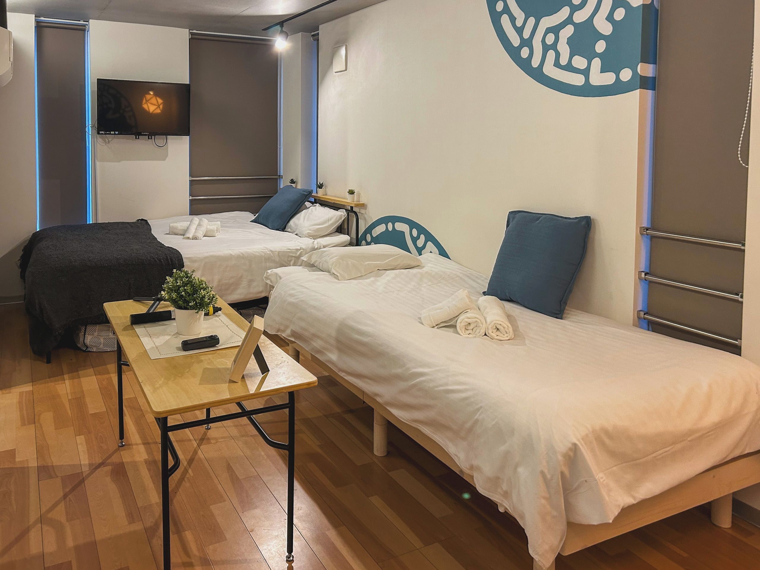 A hotel room with two single beds, a small table with a plant, and a TV mounted on the wall.