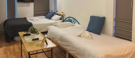 A hotel room with two single beds, a small table with a plant, and a TV mounted on the wall.