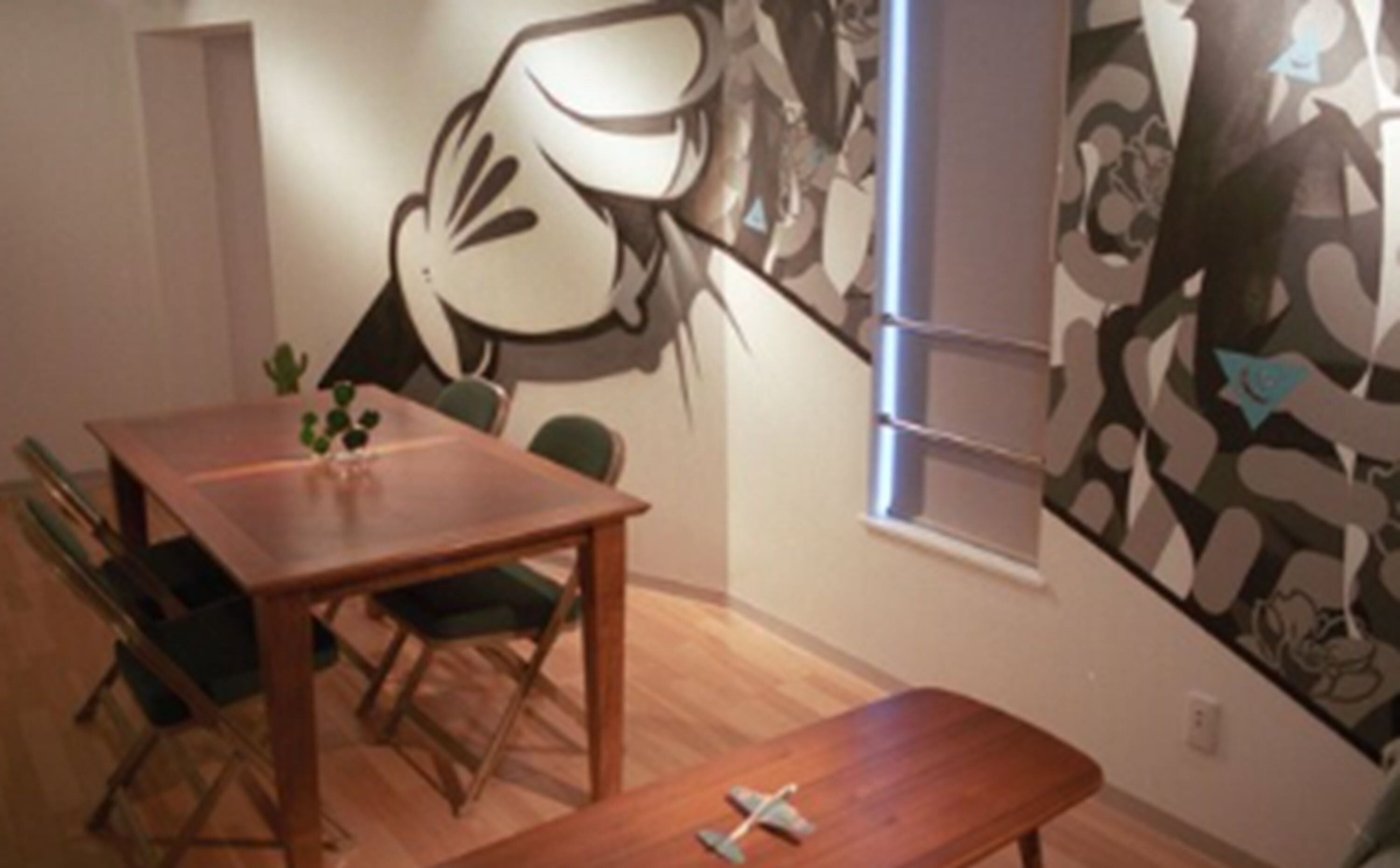 Un comedor con una mesa y sillas de madera, una planta pequeña sobre la mesa y un cuadro abstracto grande en la pared.