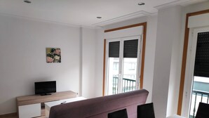 A modern living room with a sofa, a TV, a small table, and a balcony with a railing. - Apartamentos Revolta Sanxenxo 3000 (Sanxenxo)