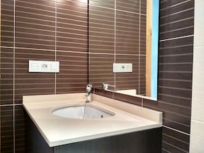Une salle de bain moderne avec un lavabo rectangulaire, un miroir et des murs recouverts de carreaux marron.