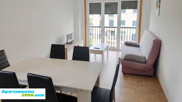 A dining area with a table and chairs, a sofa, and a balcony with a view of buildings. - Apartamentos Revolta Sanxenxo 3000 (Sanxenxo)