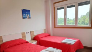 A hotel room with two beds, each with red bedding and white towels, a small painting on the wall, and a window with a view of greenery. - Apartamentos Revolta Sanxenxo 3000 (Sanxenxo)