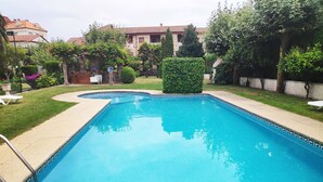 A rectangular swimming pool with a blue interior, surrounded by a low brick wall and a well-maintained lawn. - Apartamentos Revolta Sanxenxo 3000 (Sanxenxo)
