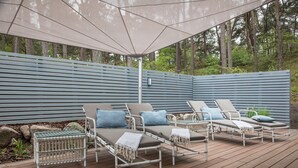 A deck with lounge chairs and a table, surrounded by a blue fence and trees. - Upstalsboom Trassenheide (Trassenheide)