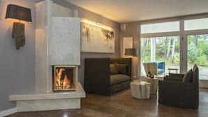 A modern living room with a fireplace, comfortable seating, and a large window offering a view of the outdoors. - Upstalsboom Trassenheide (Trassenheide)