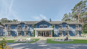 A hotel with a central entrance, two-story structure, and a landscaped front yard with seating areas. - Upstalsboom Trassenheide (Trassenheide)