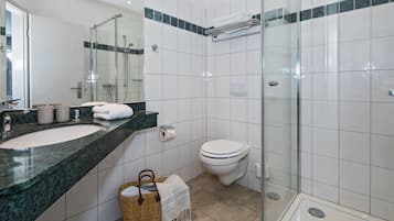 Un baño moderno con ducha de vidrio, inodoro blanco y un lavabo grande con encimera de mármol.